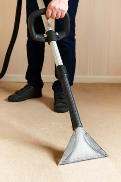 This is a photo of a man steam cleaning a cream carpet, using a professional steam cleaning machine works carried out by Chigwell Carpet Cleaning