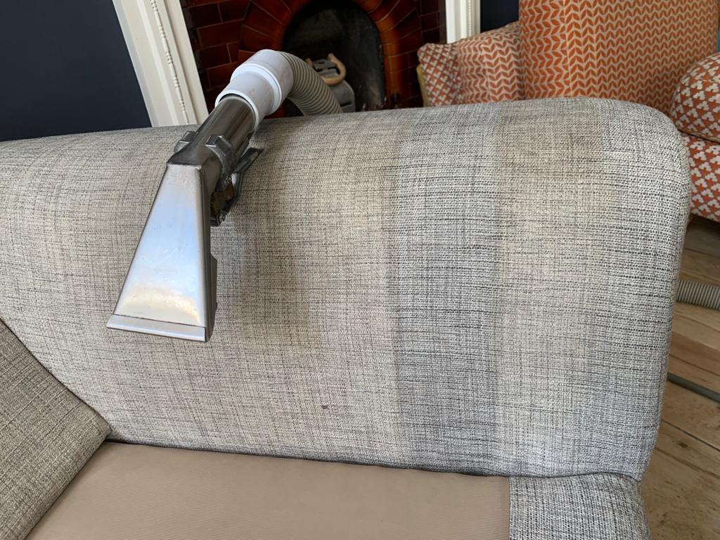 This is a photo of an arm of beige sofa that shows a test patch that has been steam cleaned. The steam cleaning machine is also showing in the photo works carried out by Chigwell Carpet Cleaning