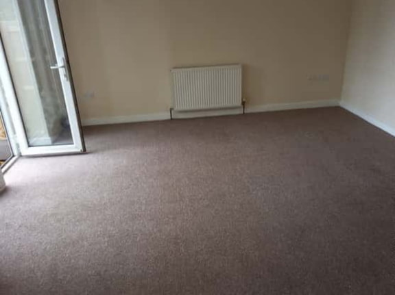 This is a photo of a living room after it has been cleaned. The room is empty and has a brown carpet that has been steam cleaned works carried out by Chigwell Carpet Cleaning